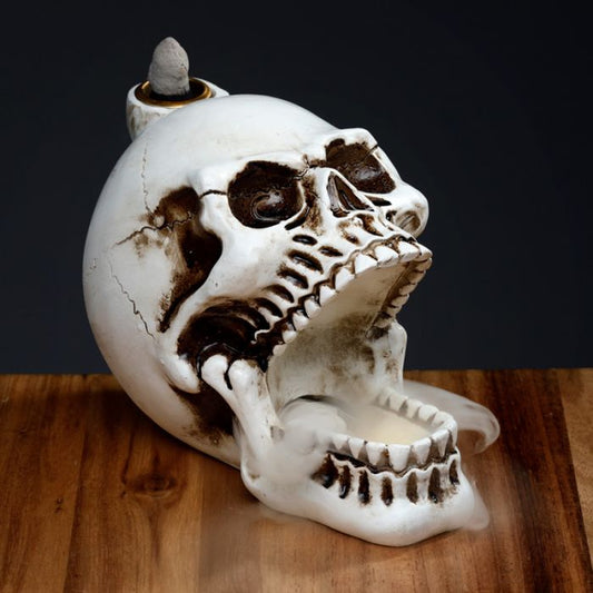Skull-shaped incense burner on a wooden surface with a dark background