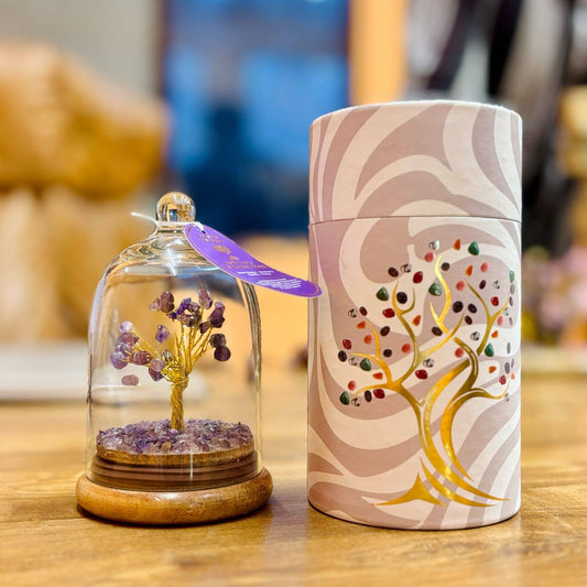 Purple gemstones on a gold wire tree in glass dome on wooden table with box at side displaying a tree picture