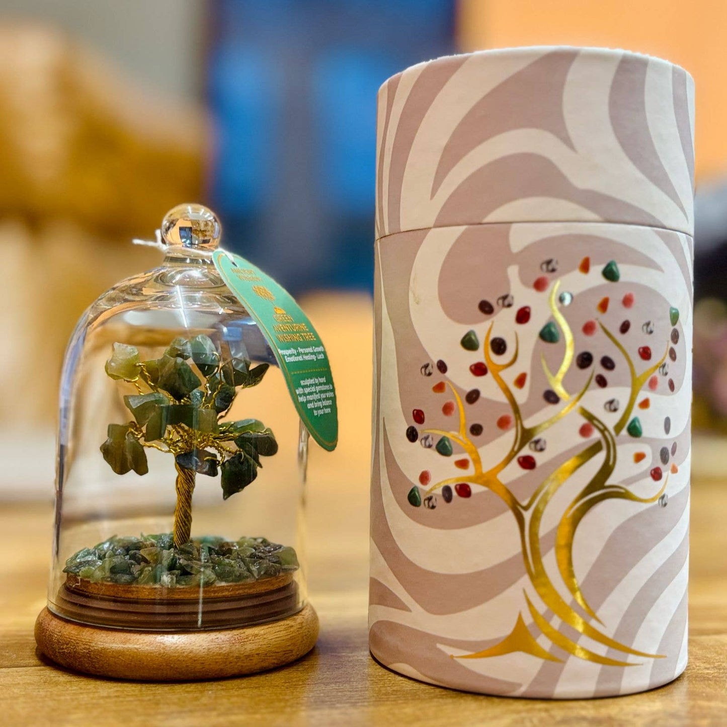 Decorative item with a tree inside a glass dome and a cylindrical container with tree design on a wooden surface.