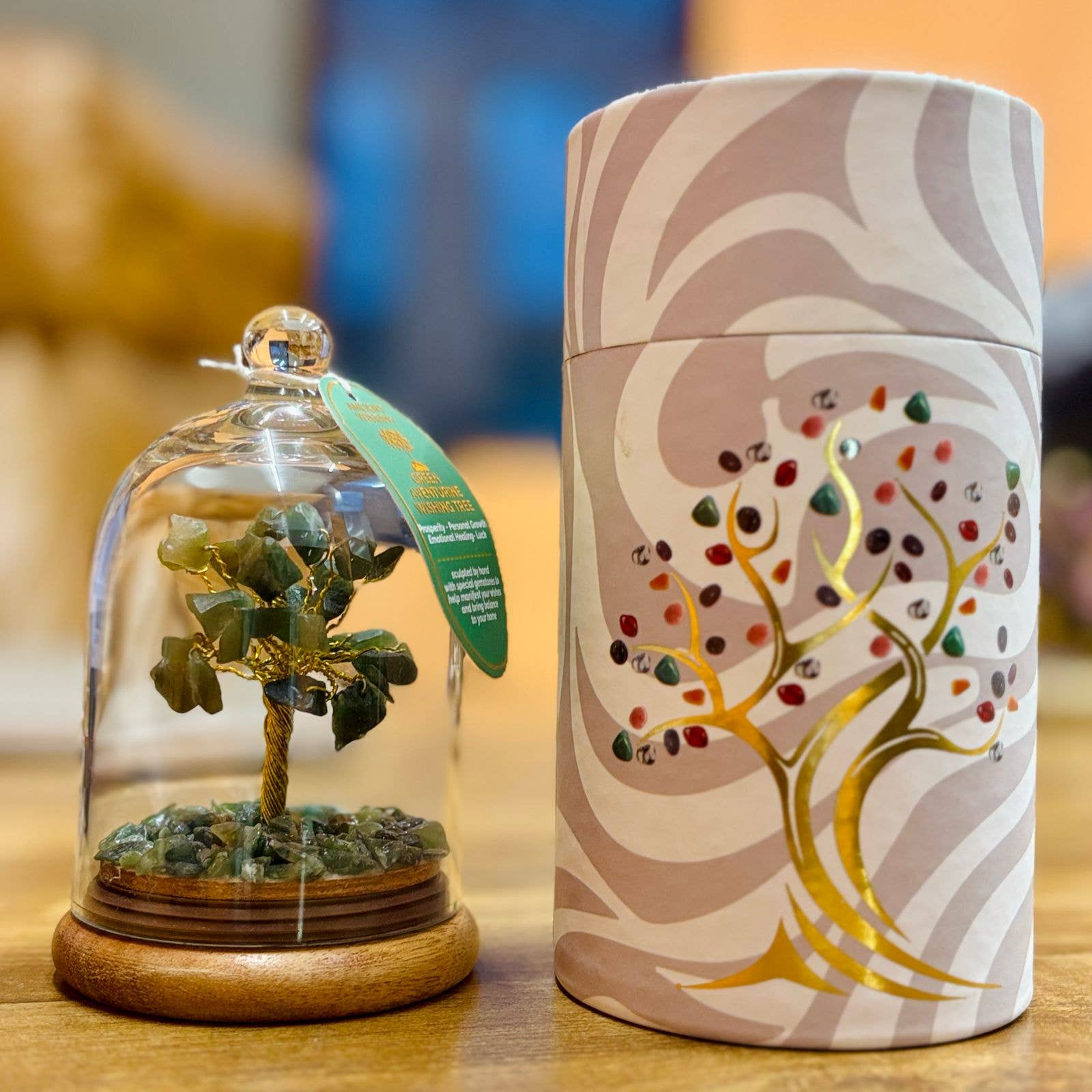Decorative item with a tree inside a glass dome and a cylindrical container with tree design on a wooden surface.