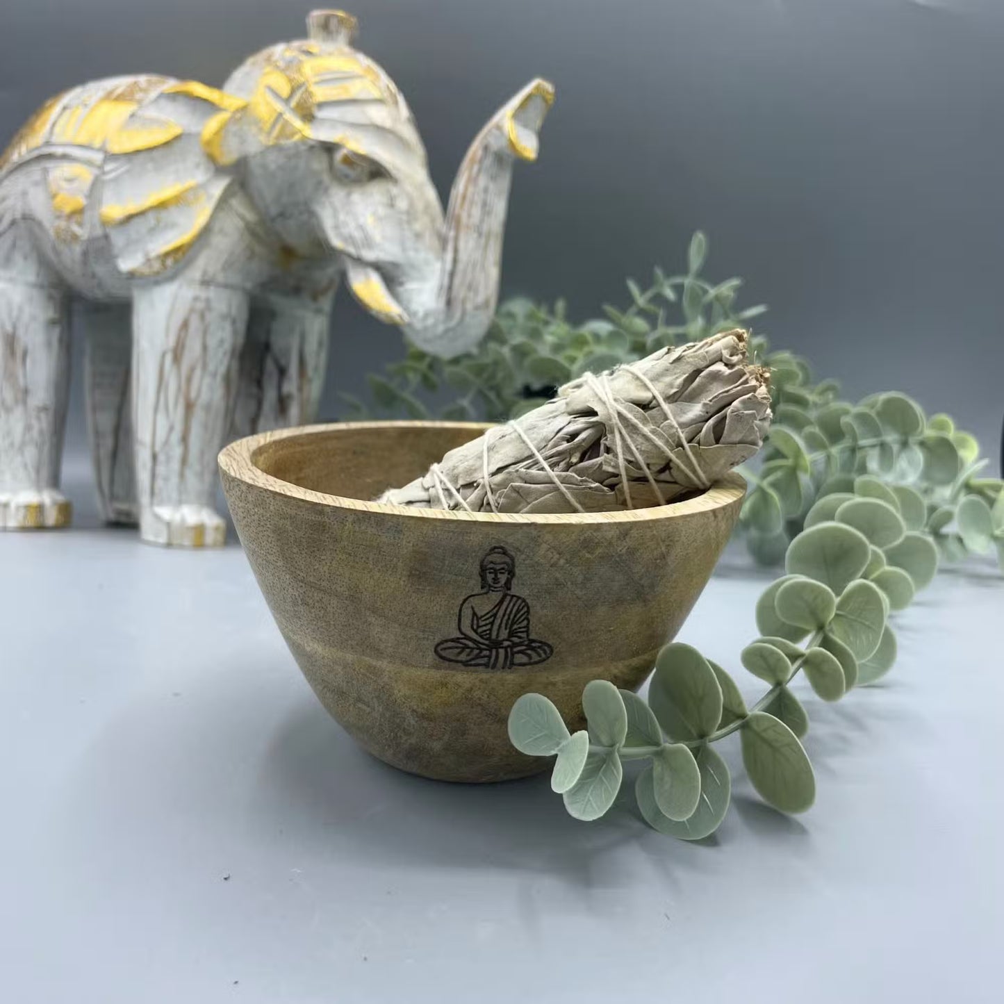 Wooden bowl with buddha design containing smudge stick on a decorative background