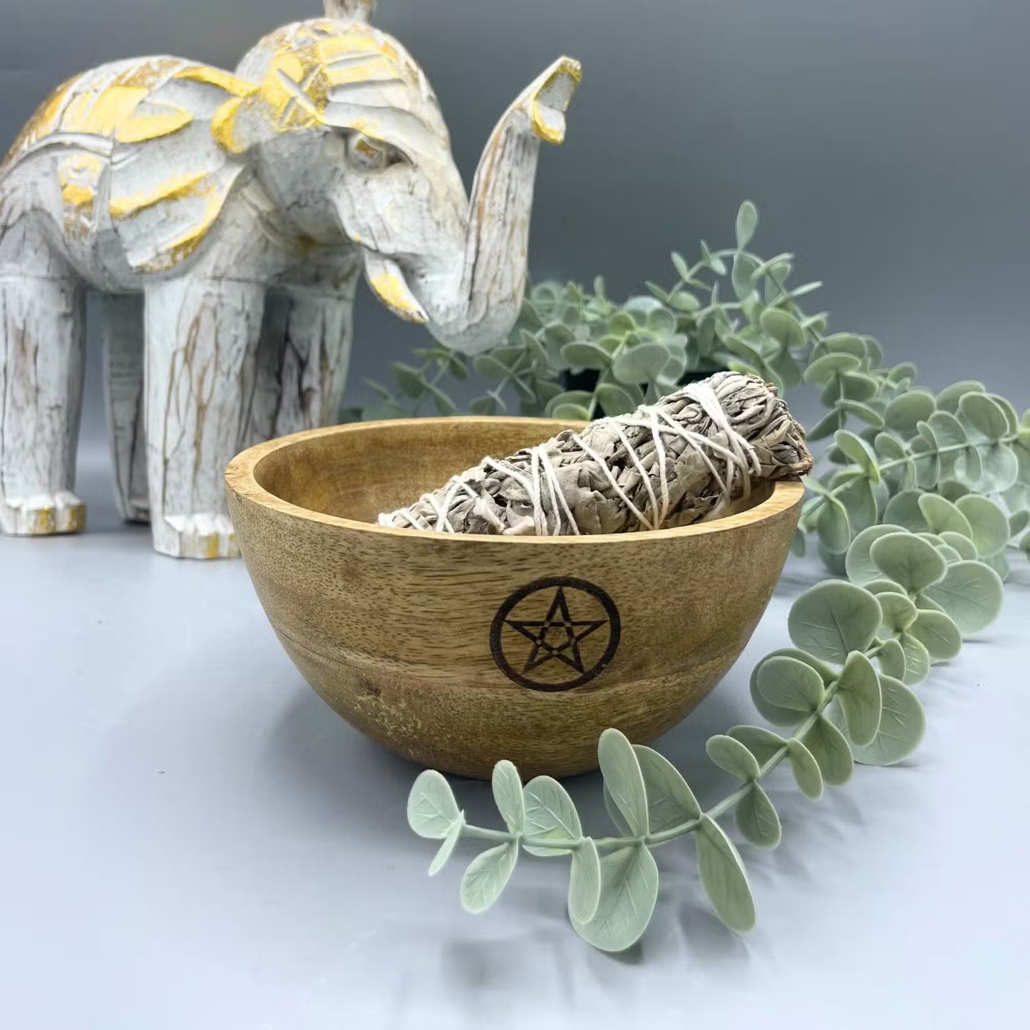 Wooden bowl with pentagram design containing a smudge stick on a decorative background