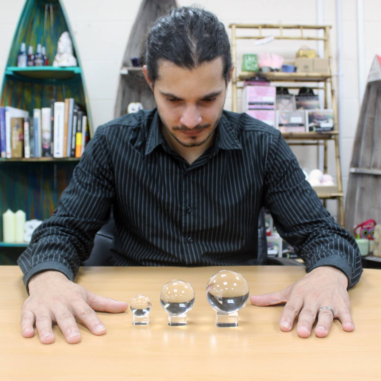 Man looking at 3 clear crystal balls on wooden table with book shelfs in background