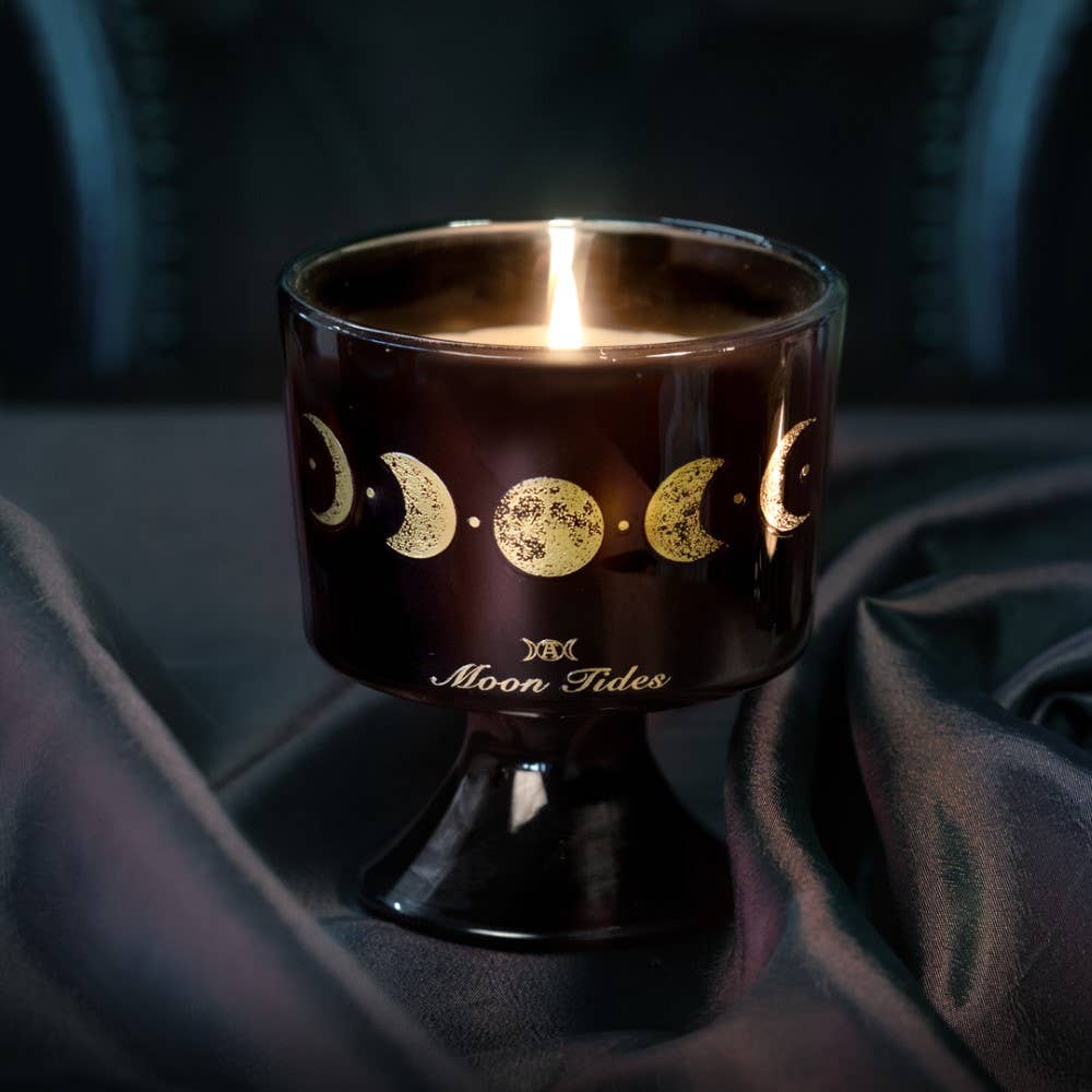 Candle in a brown holder with moon phases design on a dark fabric background