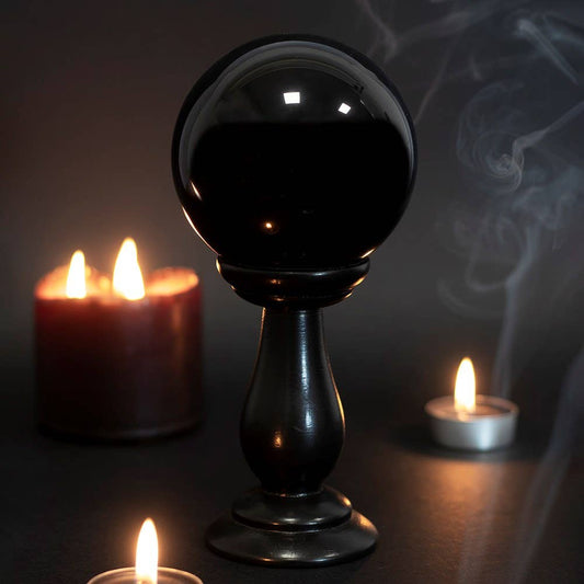 Black crystal ball on a stand with candles in the background