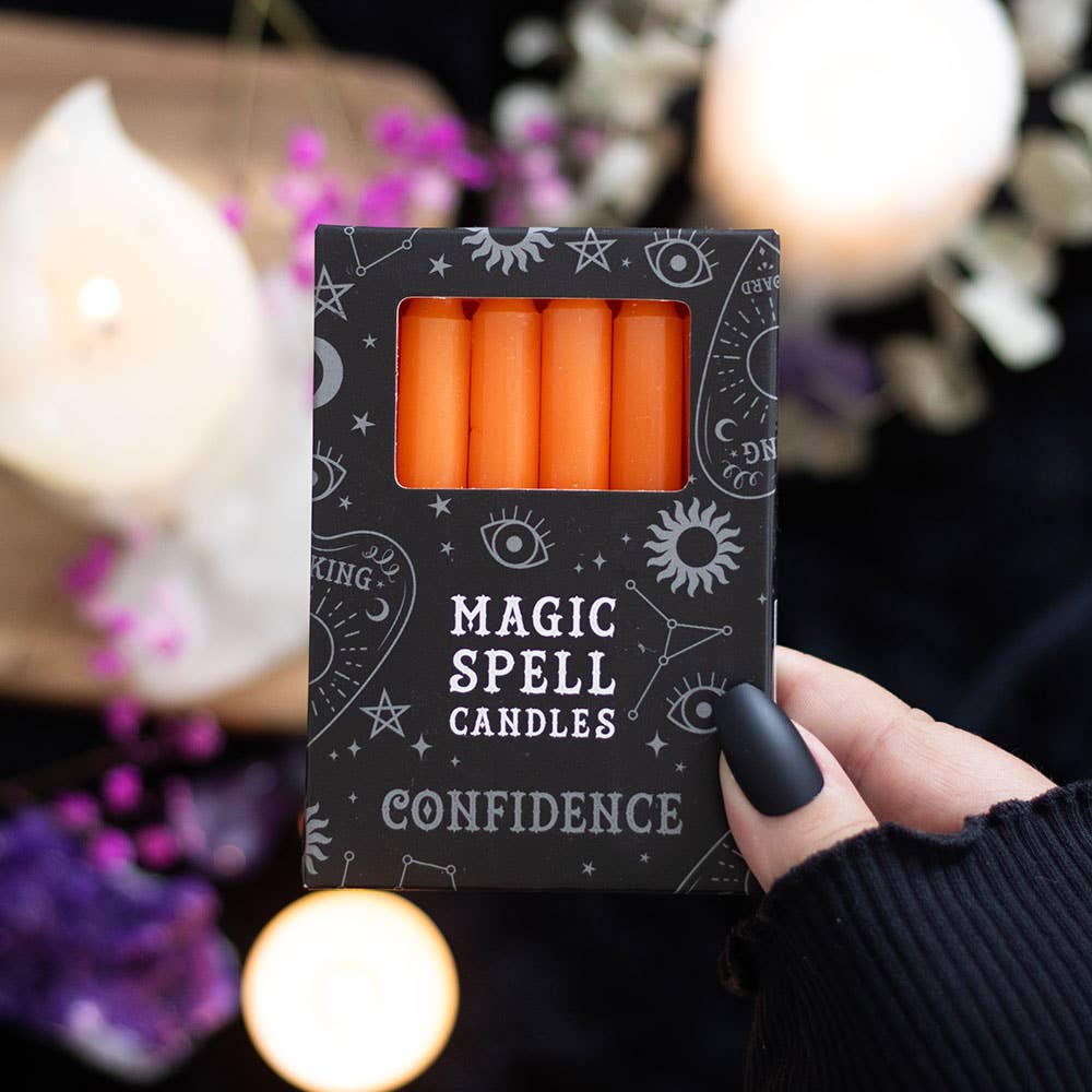 Box of 'Magic Spell Candles' labeled 'Confidence' held by a hand with a blurred candlelit background.