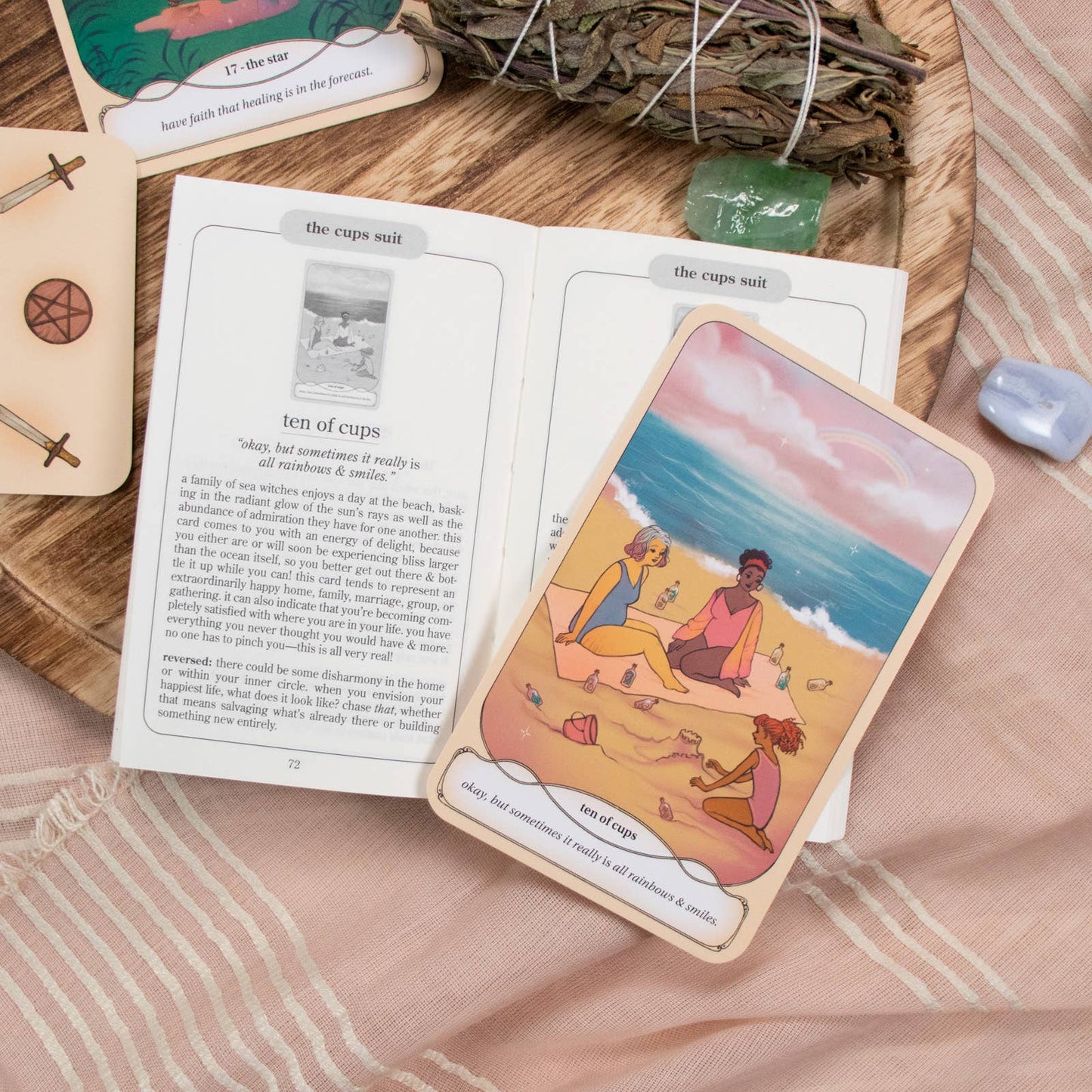 Card with a beach scene and people sitting on sand, placed on an open book with tarot cards and nature elements.