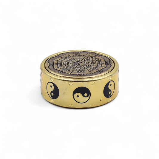 Round brass object with star and moon design on one side and yin yang symbols on the other, on a white background.