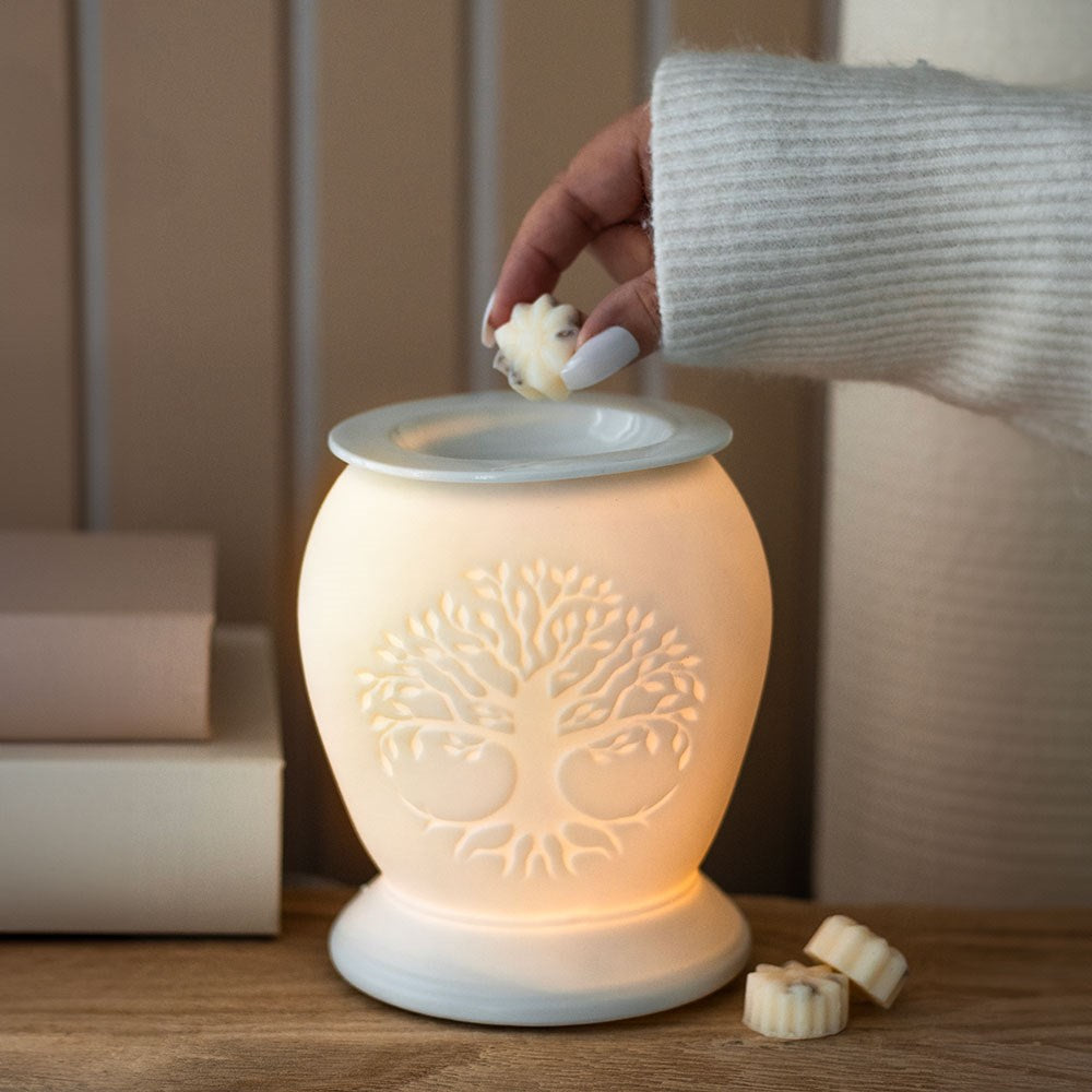 A hand using wax warmer in white ceramic with tree of life design