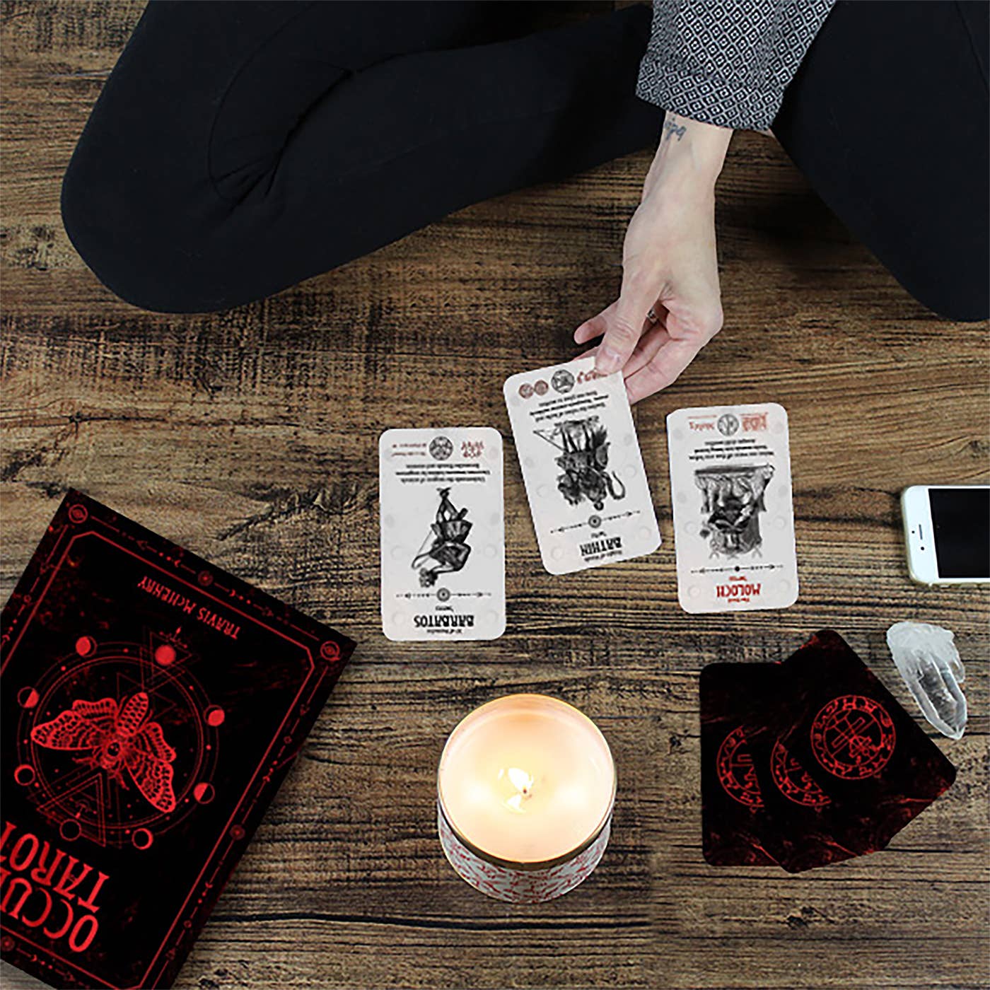 Person using tarot cards on a wooden table with a candle and phone.
