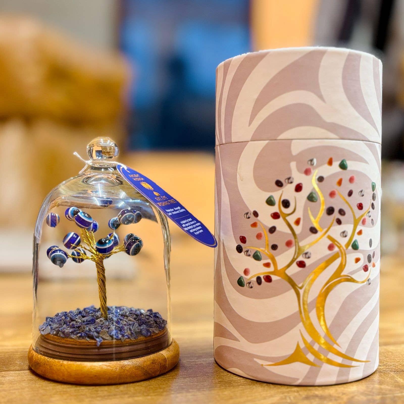 Decorative item with a tree inside a glass dome and a cylindrical container with tree design on a wooden surface.