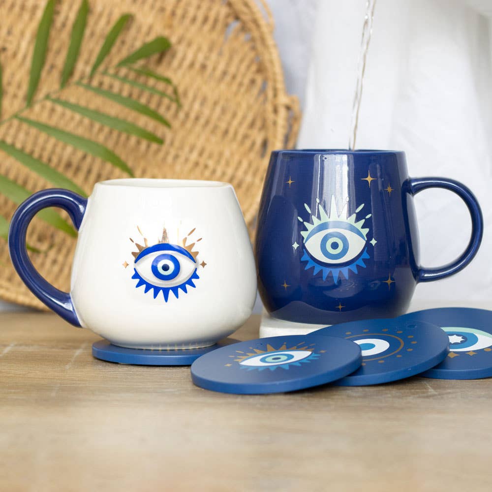 Two mugs with eye designs on a wooden surface with coasters.