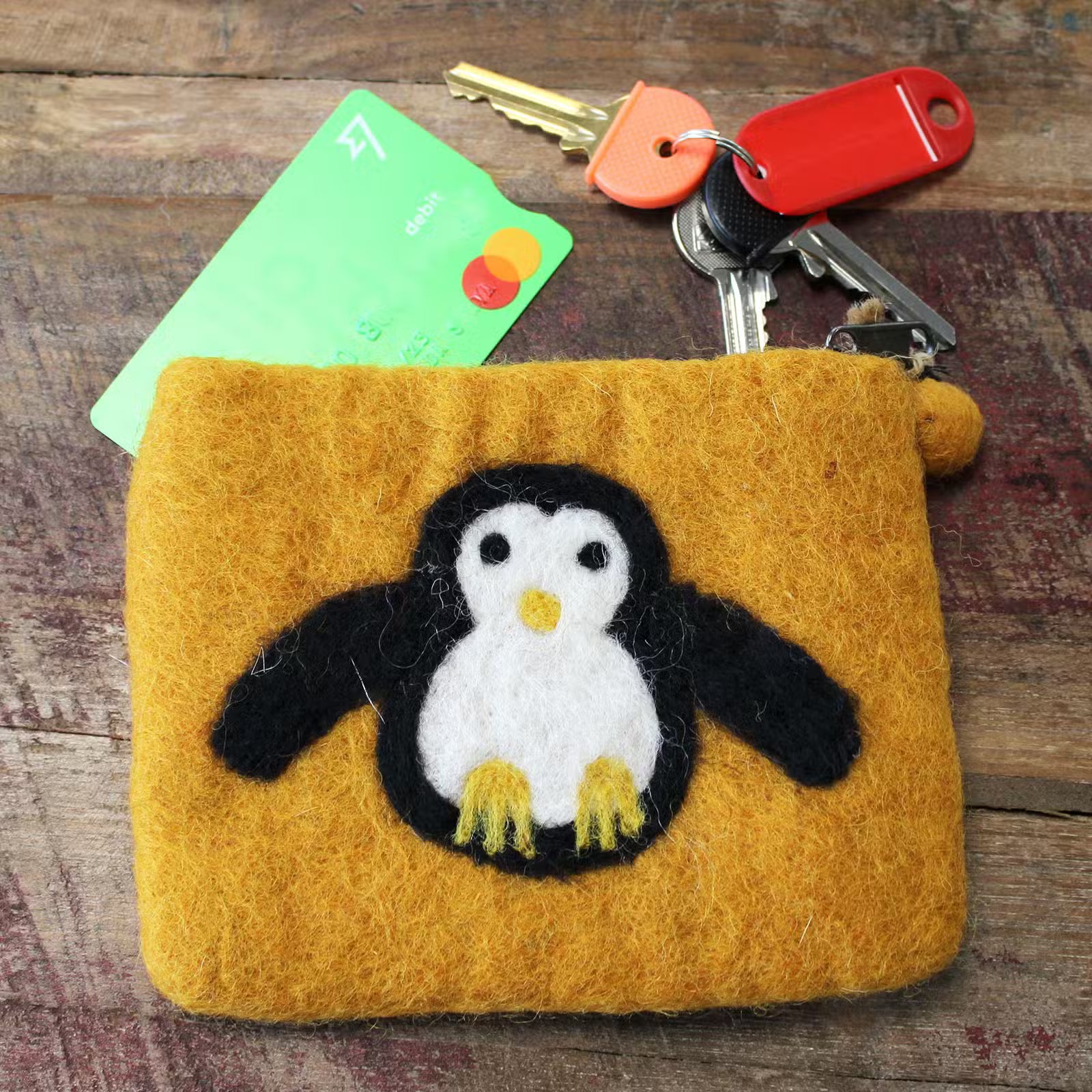 Orange felt pouch with a penguin design, keys, and a card on a wooden surface