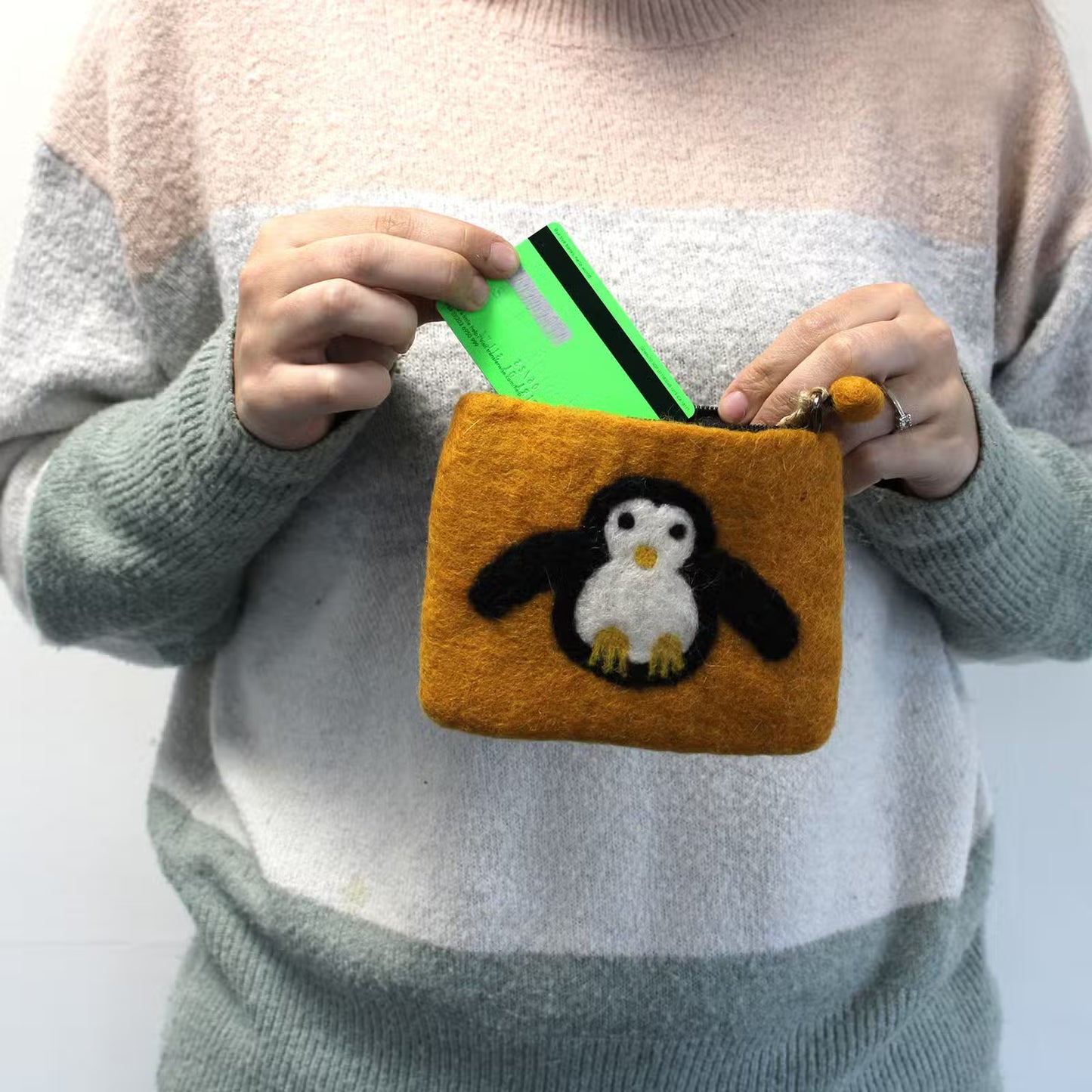 Person holding a small orange pouch with a penguin design, containing a green card.