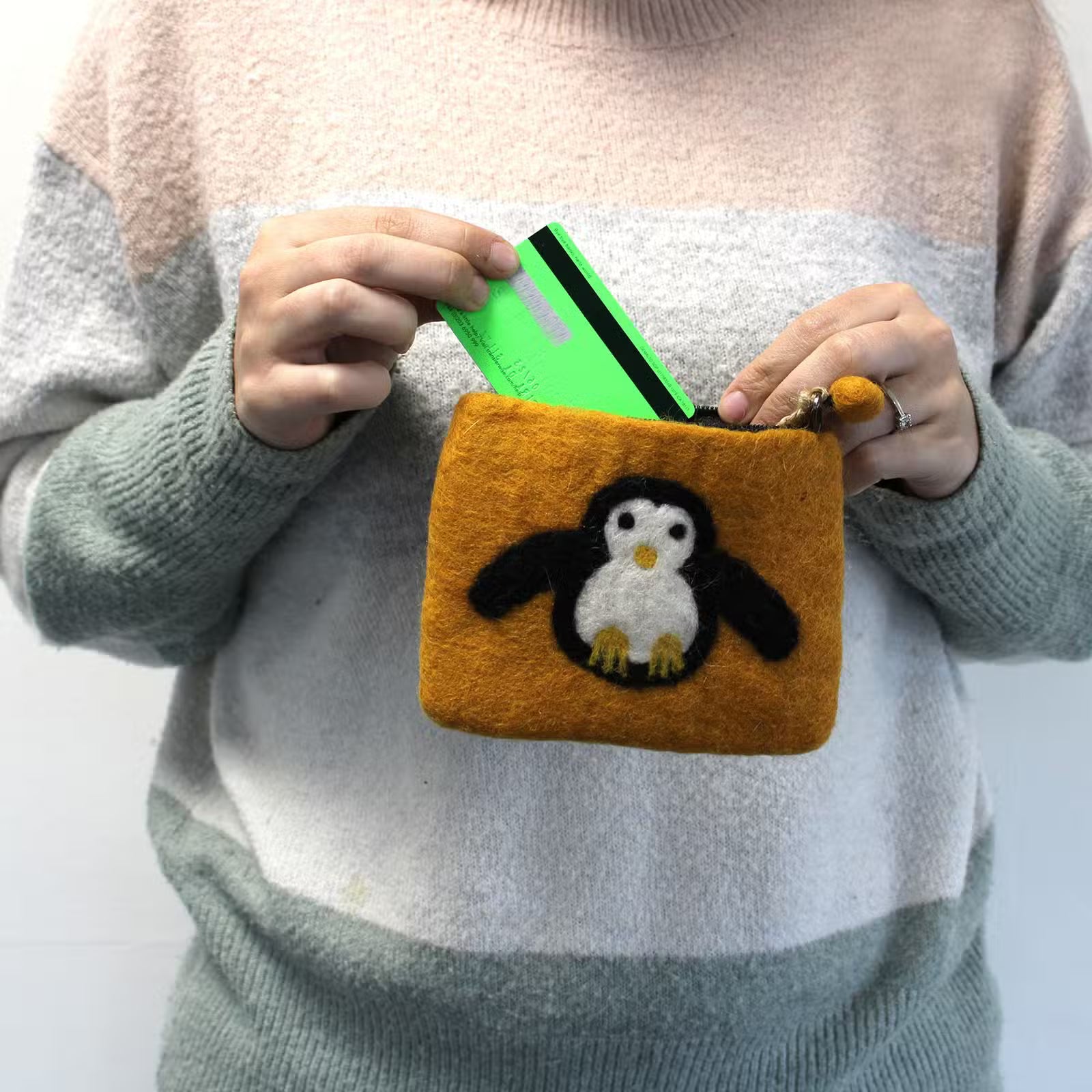 Person holding a small orange pouch with a penguin design, containing a green card.
