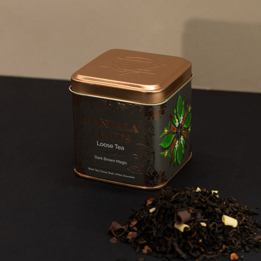 Mandala Leaves dark brown magic loose tea beside a green and gold tin