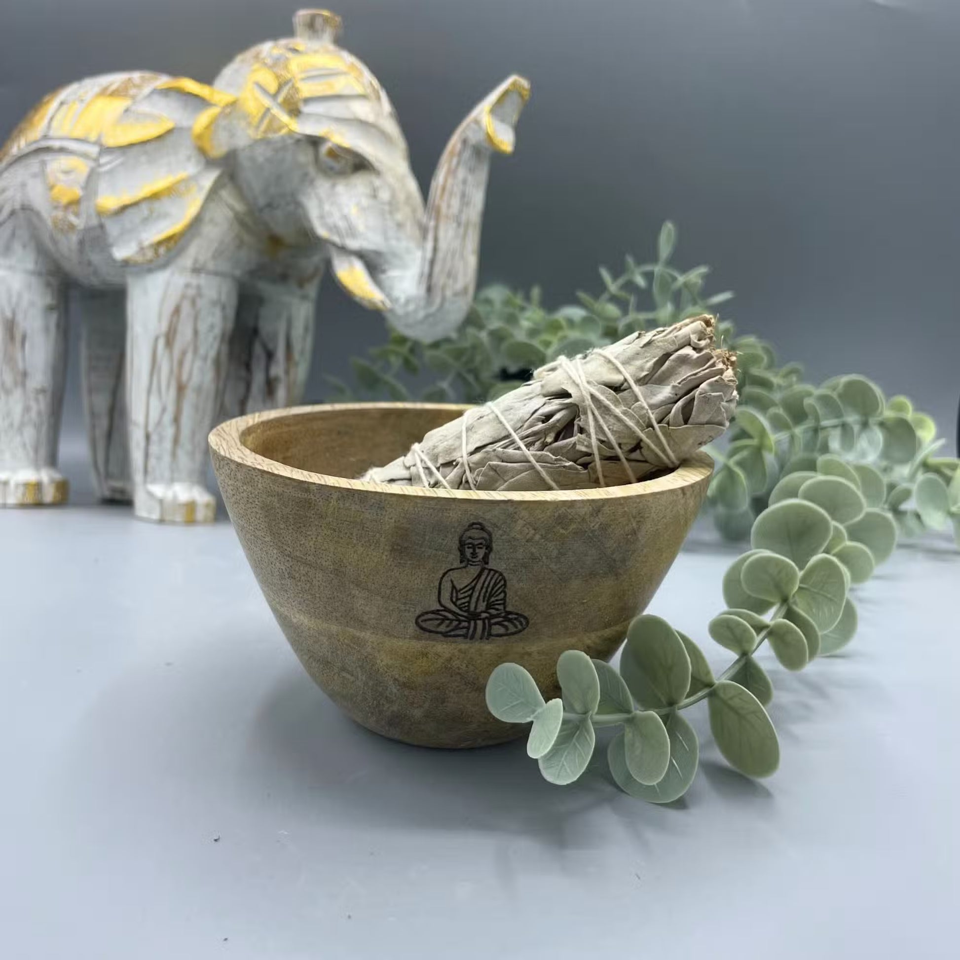 Wooden bowl with buddha design containing smudge stick on a decorative background