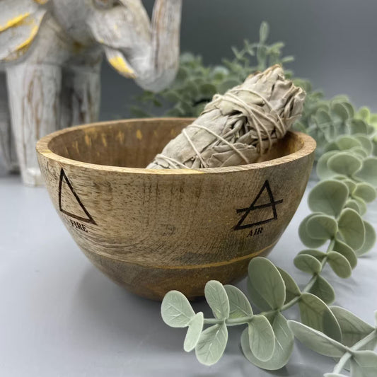 Wooden bowl with four elements design containing a smudge stick on a decorative background