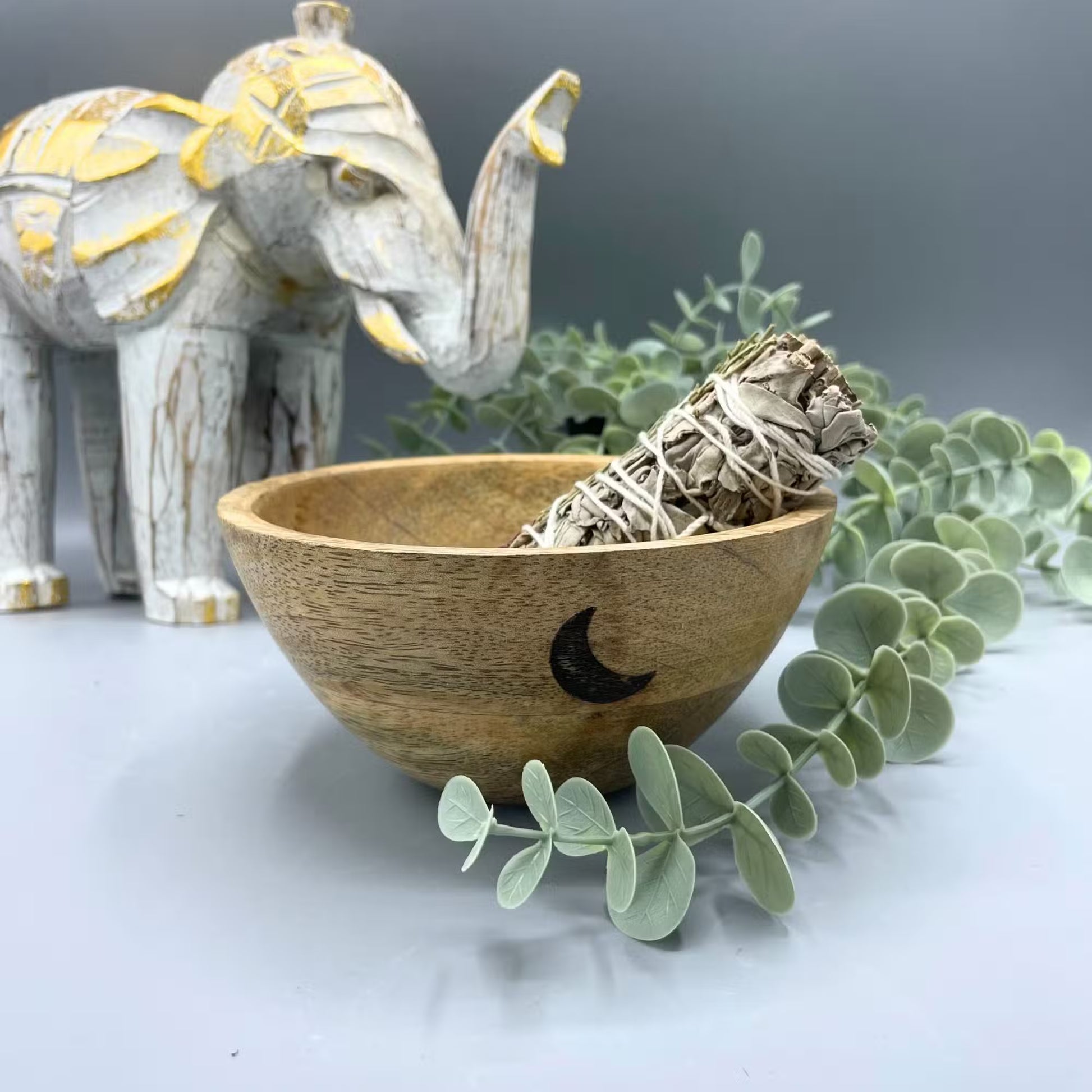 Wooden bowl with moon design containing smudge stick on a decorative background