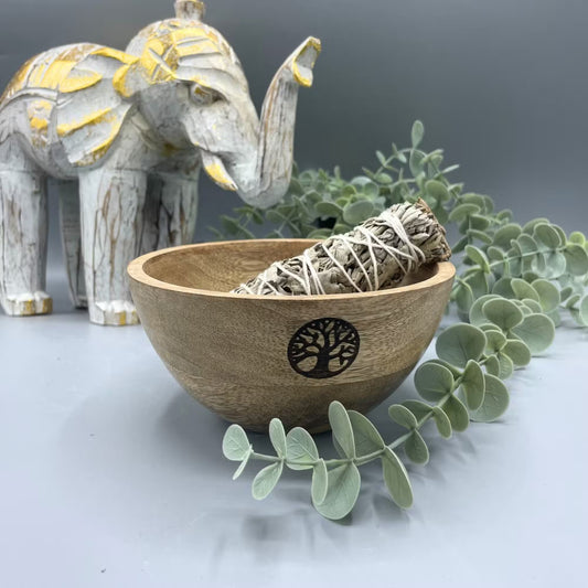 Wooden bowl with sage smudge sticks, eucalyptus leaves, and a decorative elephant on a gray background