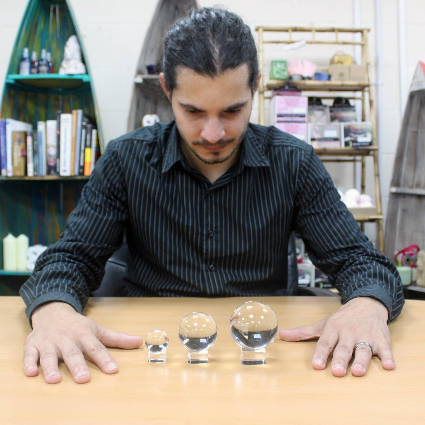 Man looking at 3 clear crystal balls on wooden table with book shelfs in background