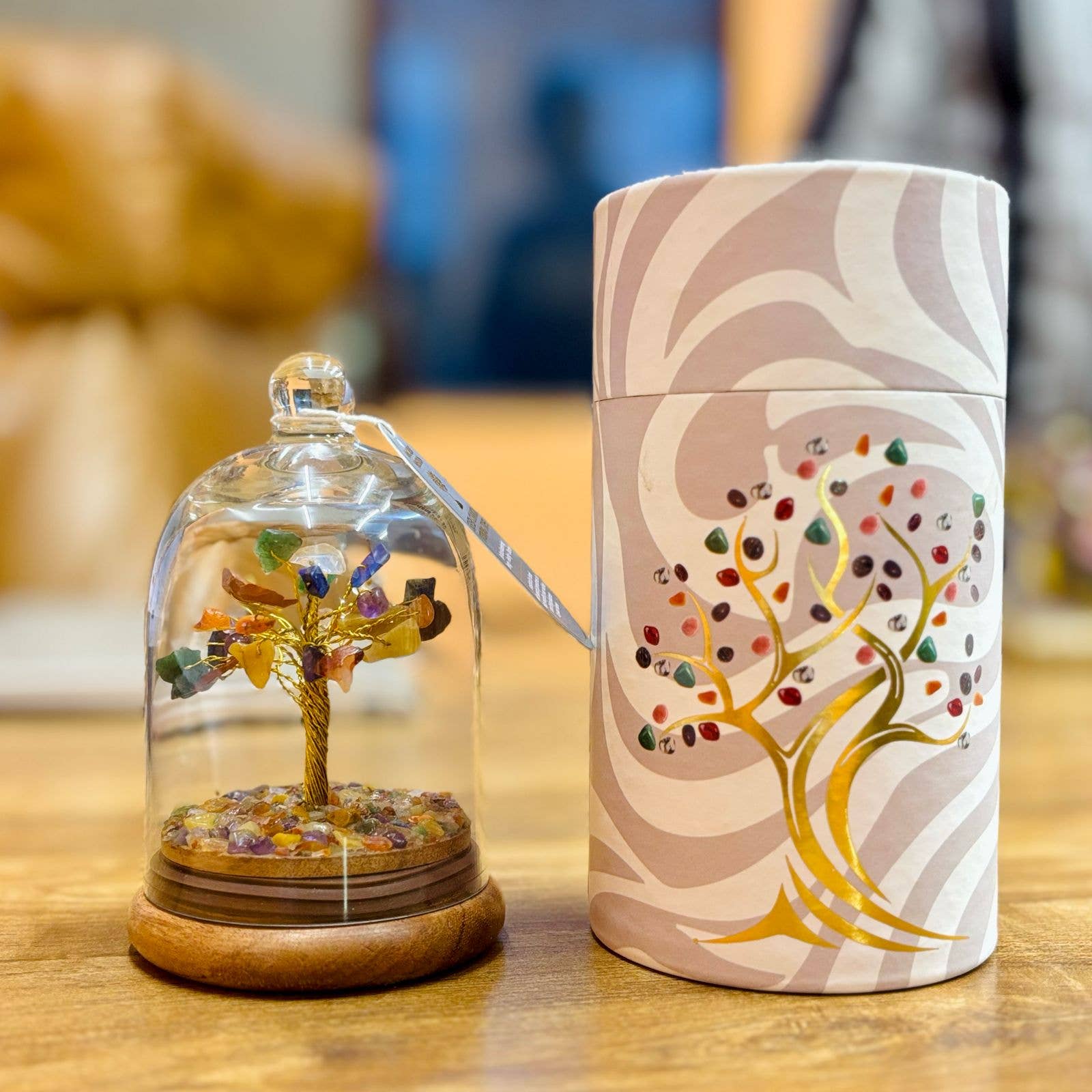 Decorative item with a tree design inside a glass dome and a matching cylindrical container on a wooden surface.