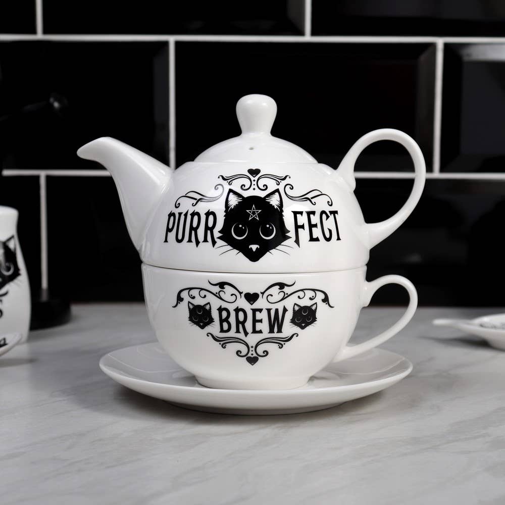 White teapot and cup set with black cat design and text on a kitchen counter.