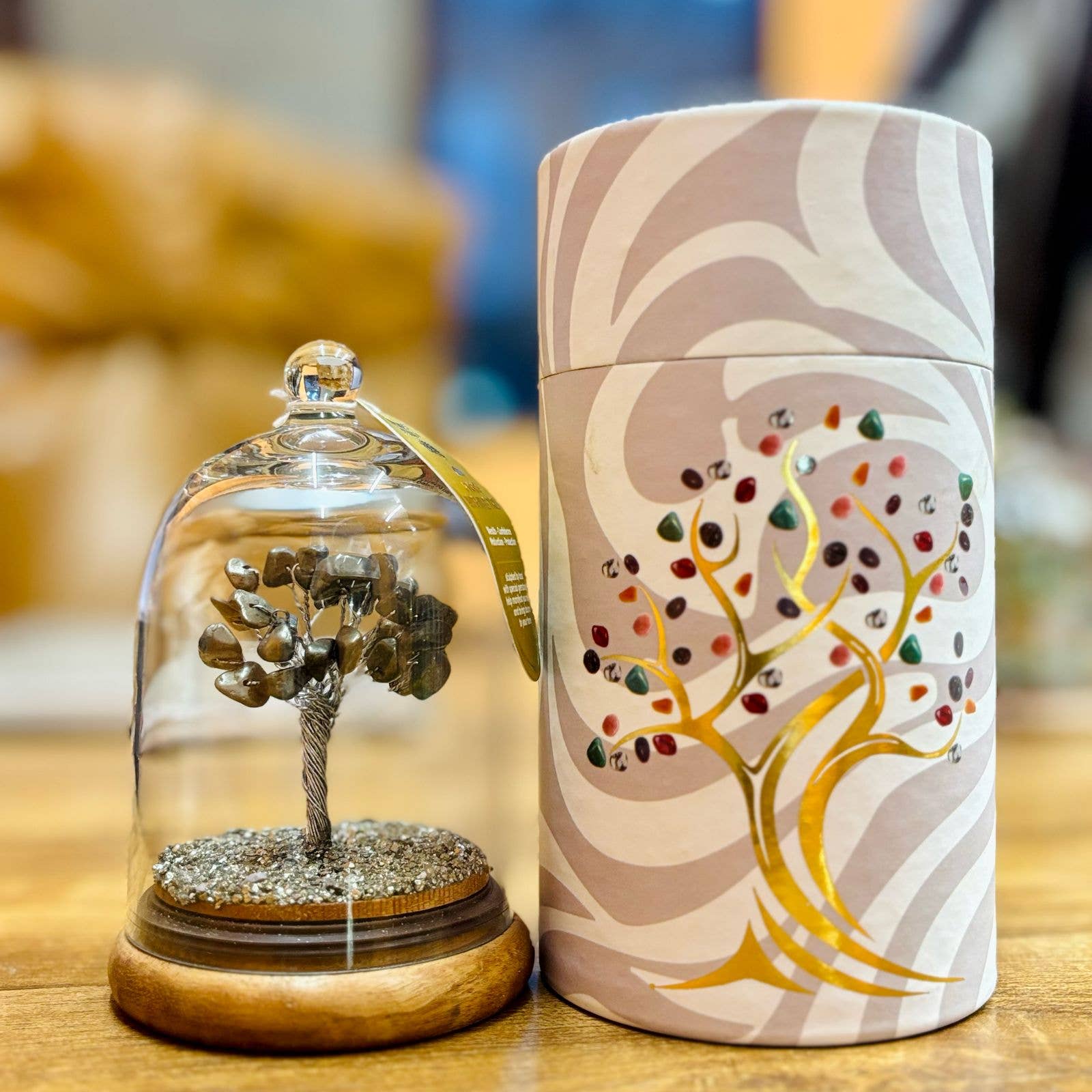 Decorative item with a tree inside a glass dome and a cylindrical container with a tree design on a wooden surface.