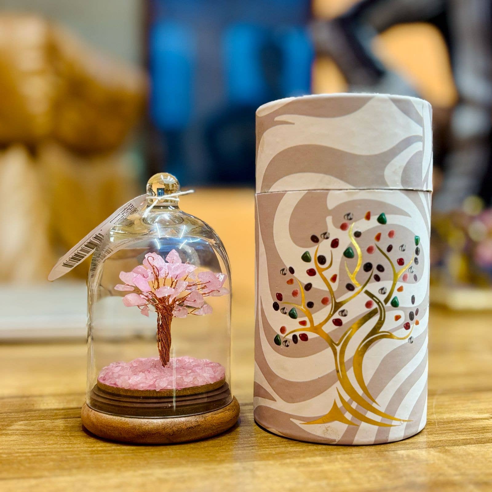 A pink gemstone tree in glass dome case on a wooden table with box at side displaying a tree