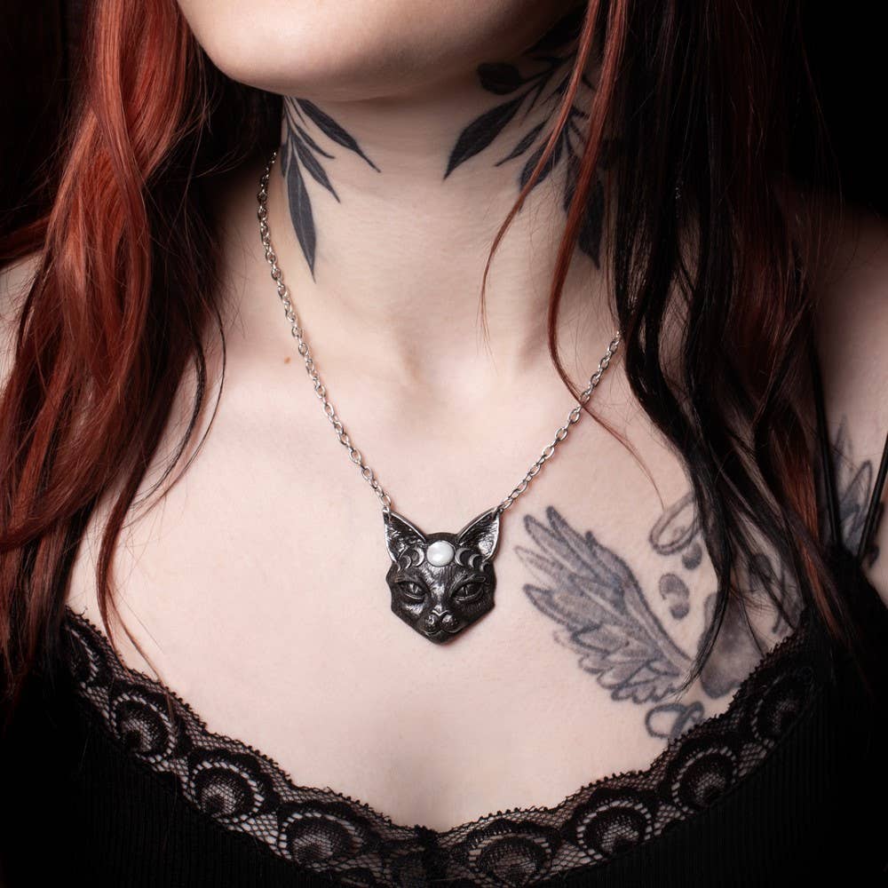 Person wearing a black cat pendant necklace with visible tattoos on neck and chest.