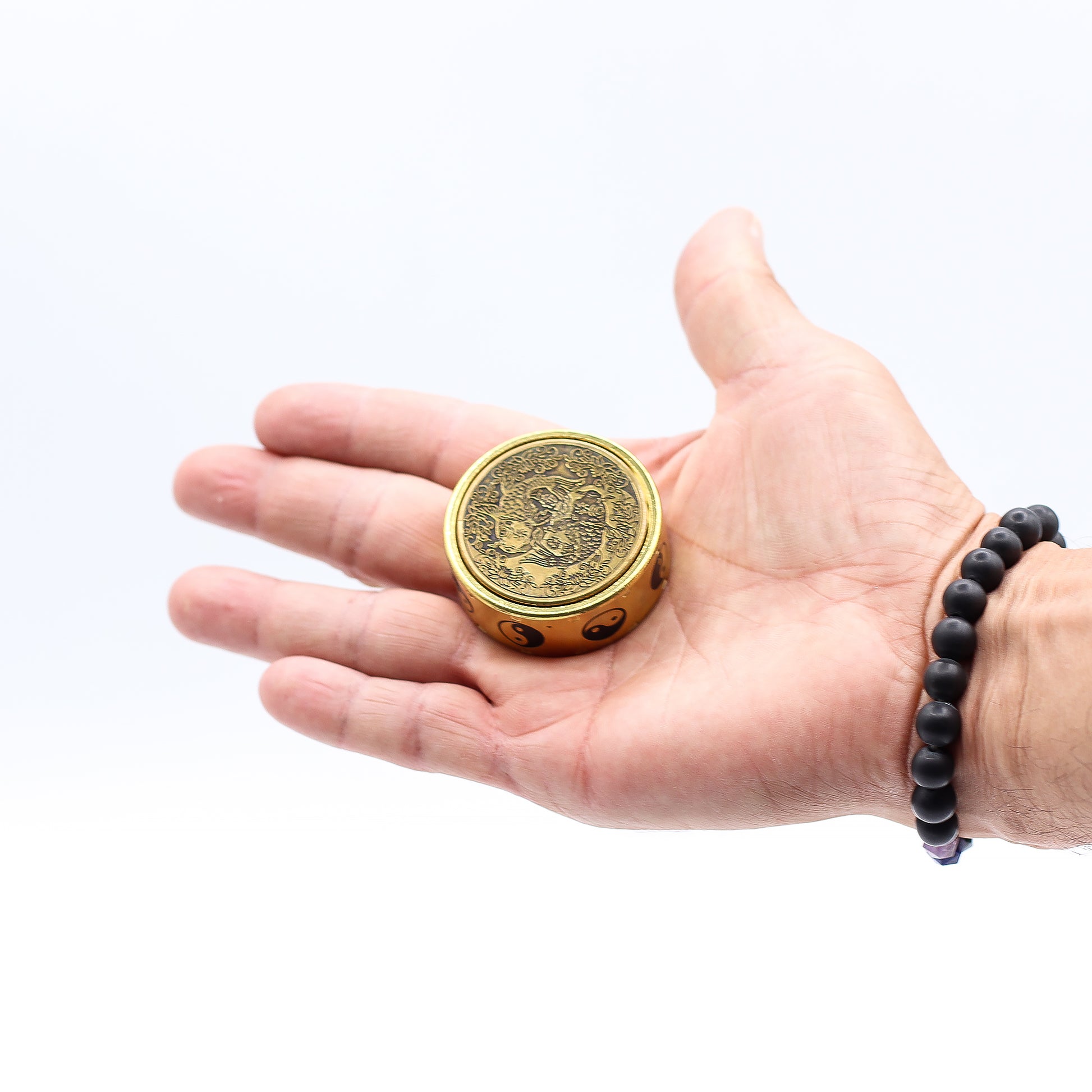 Hand holding a gold circular object with intricate designs on a white background