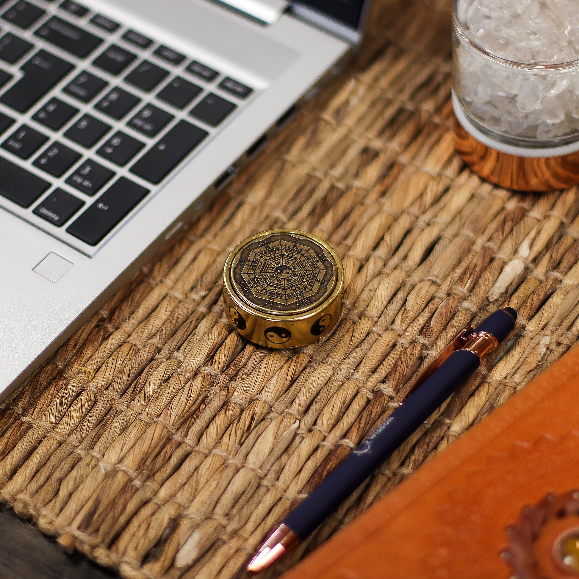 Laptop on a woven mat with a decorative object, pen, and glass of water.