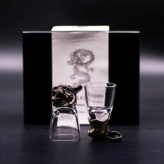 lions head shot glass next to upturned shot glass in front of gift box faded in background